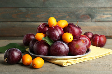 Ripe plums in metal plate on wooden background