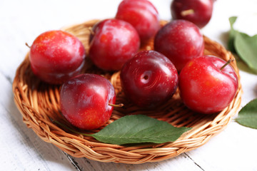 Ripe plums in wicker tray on wooden table, closeup