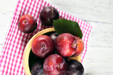 Ripe plums in bowl on wooden table with napkin, closeup