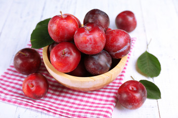 Ripe plums in bowl on wooden table with napkin, closeup