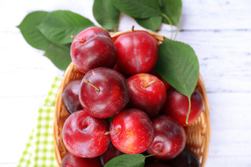 Ripe plums in wicker bowl on wooden table with napkin, closeup