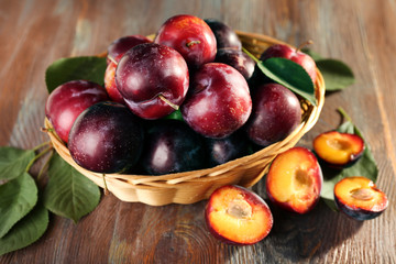Ripe plums in bowl on wooden background