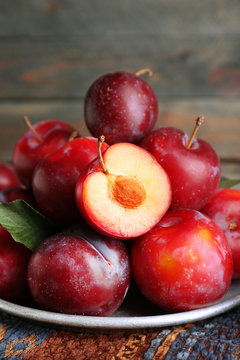 Ripe plums in metal plate on wooden table, closeup