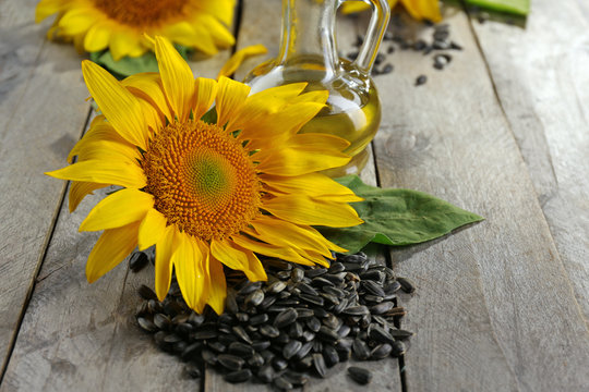 Beautiful bright sunflowers with seeds and bottle of oil on wooden table close up