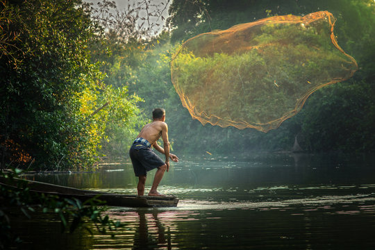 Asian fisherman fishing by net for fish in river