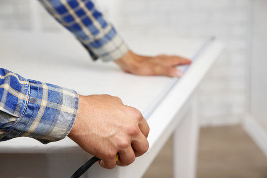 Young man measuring home furniture with measure tape, close up