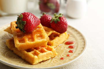 Sweet homemade waffles with fresh strawberries on plate, on light background