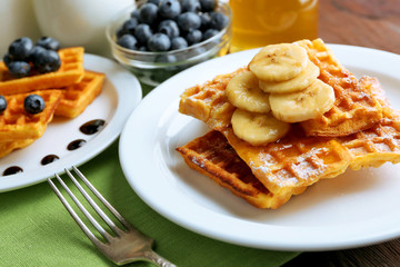 Sweet homemade waffles with sliced banana on plate, on light background