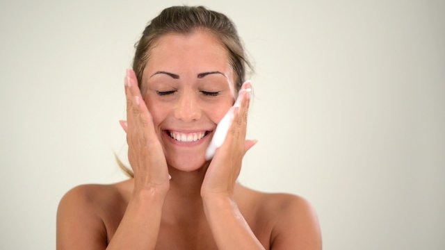 Beautiful young woman washing face with moisturizing foam