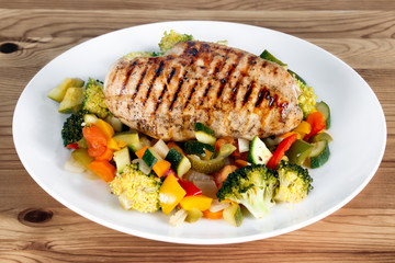 Grilled chicken fillet, breast with cooked vegetable Tomatoes, Carrots, Peppers, Courgettes, brocoli on plates.