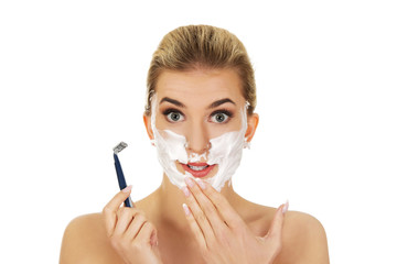 Young shocked woman shaving her face with a razor