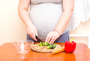 Obraz na płótnie Canvas Pregnant woman cuts the cucumber. Diet for pregnant women.