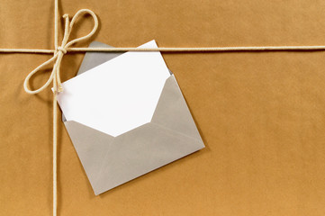 Fototapeta premium Brown paper parcel or wrapped package background with greeting card message label or gift tag in silver envelope photo