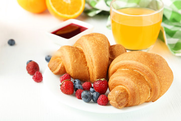 Fresh tasty croissants with berries on white wooden background