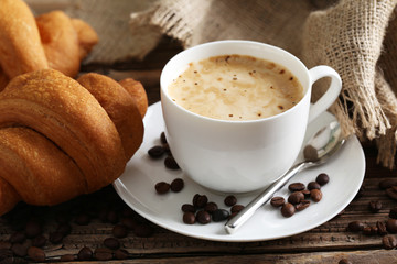 Delicious croissants with cup of coffee on brown wooden backgrou