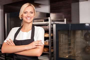 Cheerful young female cook is working in bakery