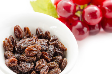 Dried raisins in white cup and fresh red grapes.