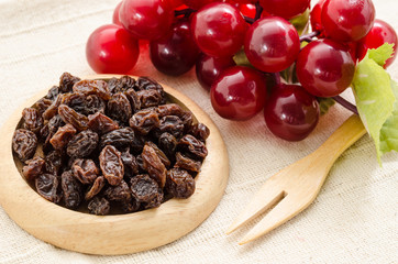 Raisins on a wooden dish and fresh red grapes.