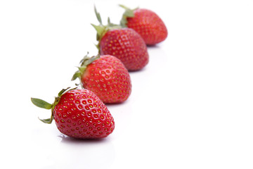 Aerial view of four Strawberries in line , front one is focused while rest are photographed out of focus , photographed against white background