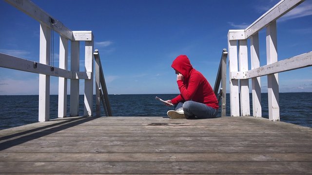 Young woman reading fanzine magazine at the edge of wooden sea pier, urban lifestyle youth, 4k uhd footage, 3840x2160