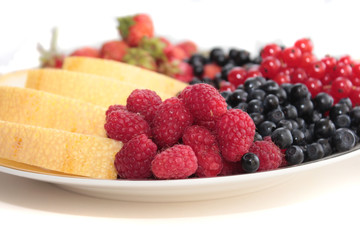A plate of fruits: raspberries on the forefround and melon, strawberries, black currants, red currants, bilberries on the background
