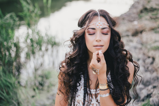 Beautiful young woman with long curly hair dressed in boho style dress posing near lake