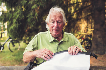 Tanned Senior Man Sitting in Forest Closing a Bag.