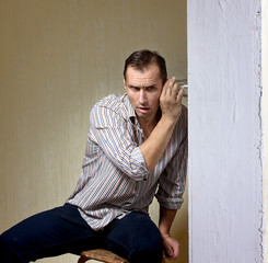 Man with a glass listening to a conversation through the wall