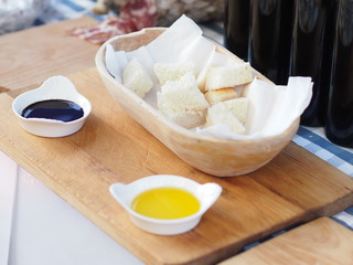 White bread in a wooden bowl and two different samples of vinegar / oil / dressings in white porcelain bowls.