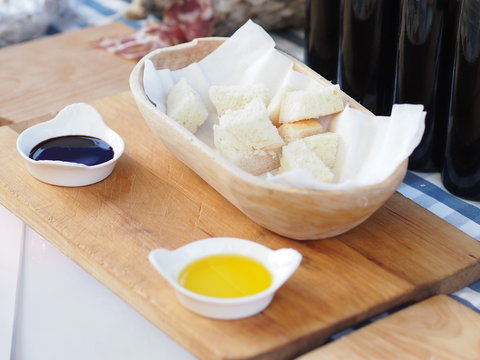 White bread in a wooden bowl and two different samples of vinegar / oil / dressings in white porcelain bowls.