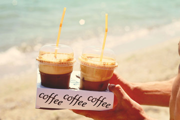 Male hands holding two ice frappe coffee on the beach near sea