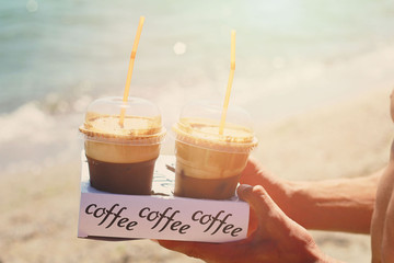 Male hands holding two ice frappe coffee on the beach near sea