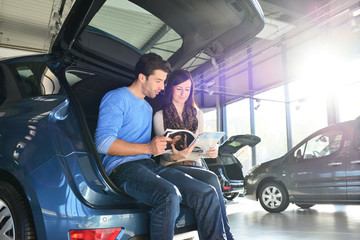 Plakat junges Paar schaut sich eine Werbebroschüre im Autohaus an - Autokauf und Besichtigung im Showroom 