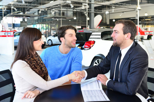 Vertragsabschluss im Autohandel - junges Paar kauft einen Neuwagen - Handschalg mit dem Verkäufer