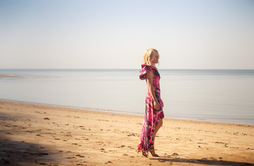 blonde girl in purple dress walks on beach