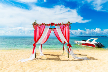 Wedding ceremony on a tropical beach in red. Arch decorated with