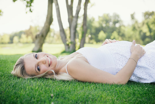 Pregnant smiling woman lie on the grass in the park