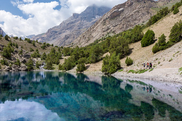 Blue Lake Landscape. Mountain Lake View and Group of People Walking on Footpath beside Water Shore