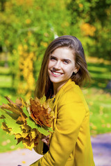 Happy young woman in yellow coat in autumn street