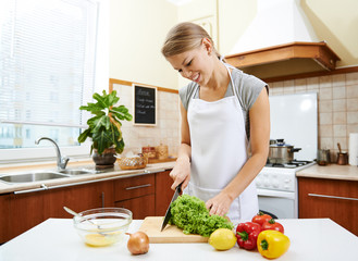 Cheerful girl cutting fresh salad in cuisine indoors. Dieting concept. Healthy lifestyle.