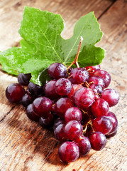 Round purple grapes with leaves on the old wooden table, selecti