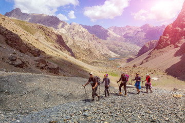 Diverse group of hikers in mountain terrain People walking along rocky footpath positive faces trekking gear poles sporty clothing bright panorama blue sky sunny day background