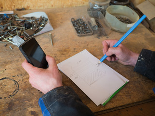 Hände eines Tischlers mit Smartphone, Zeichnung und Bleistift