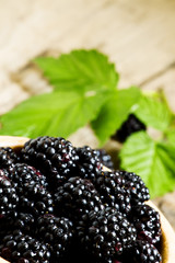 Fresh blackberries with leaves in a wooden bowl, selective focus