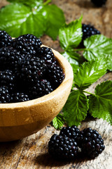 Fresh blackberries with leaves in a wooden bowl, selective focus