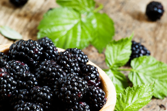 Fresh blackberries with leaves in a wooden bowl, selective focus