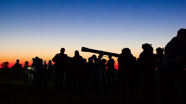 silhouettes of a group of astronomers look at the sky through a telescope time Lapse