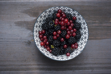 bowl with wild backberries and redcurrants on a wooden table