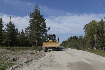 A parked grader on a road with some trees