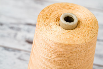 Spool of Synthetic Orange Thread on White Wooden Background